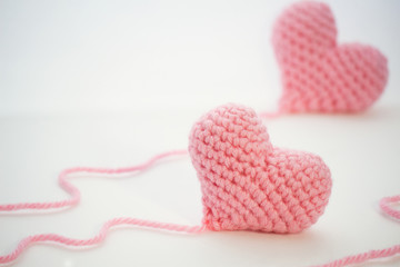 Two crochet hearts handmade from a pink thick wool yarn.The thread is not cut and still attached to the heart.