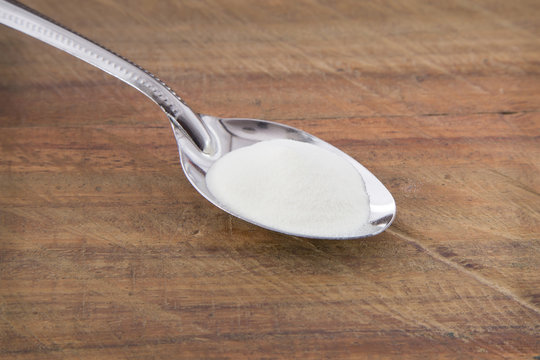 Collagen protein powder on a tablespoon against rustic wood