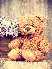 Bunch of flowers and a teddy bear on wooden background.Toned image