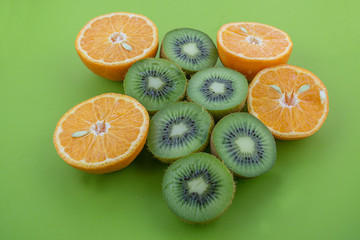 Fototapeta na wymiar Oranges and kiwis cutted on half on green surface