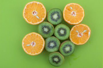 Oranges and kiwis cutted on half on green surface