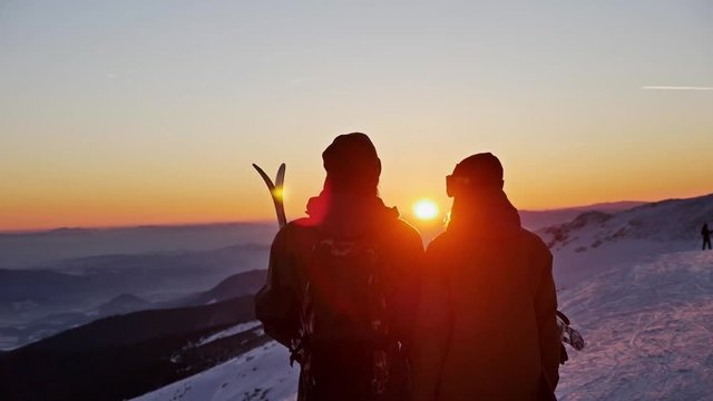 Slowmotion footage of a skier and snowboarder admiring a beautiful sunset.