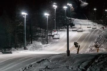  Scenic night view of an illuminated snowy ski track with a chair ski lift. Night skiing service at Sochi Gorky Gorod winter mountain resort © Wilding