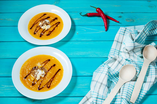 Two portions of pumpkin soup on a blue wood background