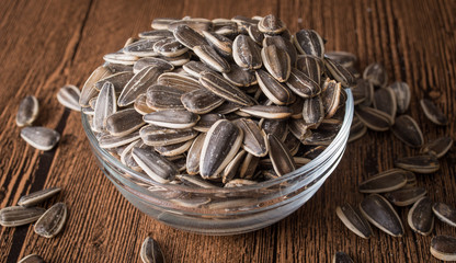 a bowl of sunflower seeds on a wooden background