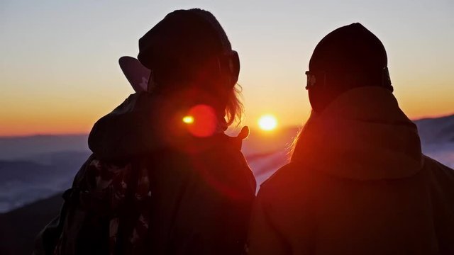 Slowmotion footage of a skier and snowboarder admiring a beautiful sunset.