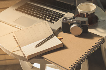 Laptop and pen on notebook beside camera,coffee cup upstairs table