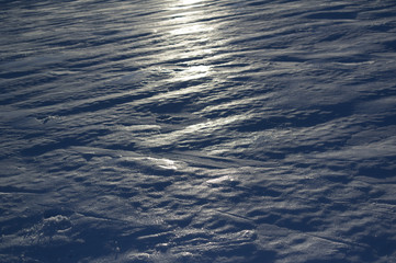 Detail of ice and snow with tracks and imprints. . Light of sun is reflecting on the surface. Backlight underexposure