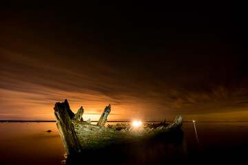 Old broken boat wreck on the shore, a frozen sea and beautiful golden sunset background. Estonia, Europe.