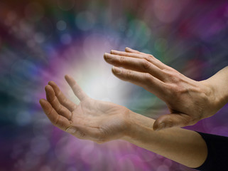 Sensing Paranormal activity - female hands sensing white energy  orb between hands on a dark multicolored bokeh background with copy space all around