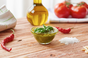 Pesto sauce on wooden table surrounded by oil, tomatoes, peppers, salt