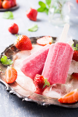 Homemade strawberry popsicles on metal plate with ice and berries. Summer food concept.