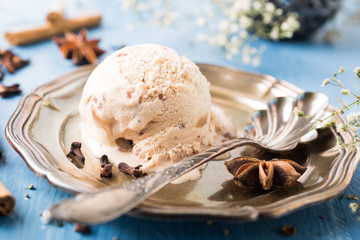 Scoop of homemade ice cream with cinnamon, apple syrup and spices on metal plate on blue wooden background. Summer food concept.
