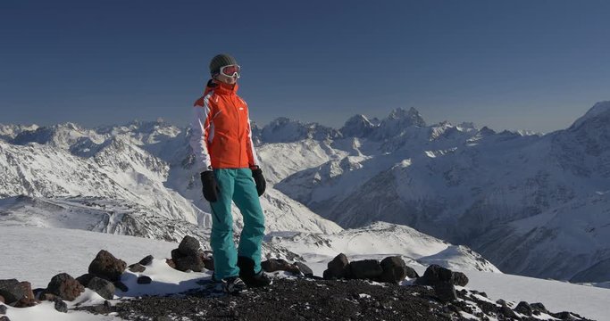 Female skier standing on top of the mountain and enjoying the view of winter landscape