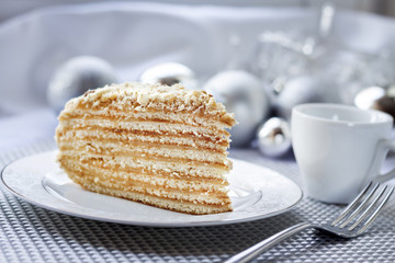 Piece of layer cake on a plate with Christmas balls on the background