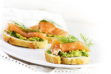  smoked salmon and avocado cream or guacamole on baguette slices, white plate