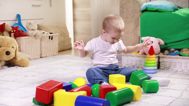 Playful little boy plays with colored blocks at home sitting on the living room floor
