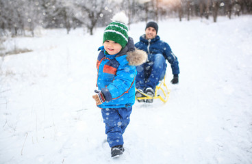 Fototapeta na wymiar Father and son sledding in winter park. Bright clothes.