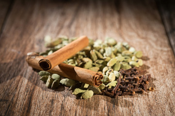 Green cardamom pods with cinnamon sticks and cloves on rustic wooden background, shallow depth of...