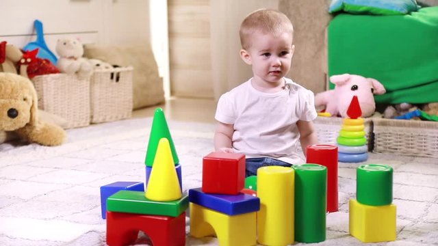 Little baby boy playing with lots of colorful plastic blocks indoor
