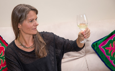 Middle aged woman on a couch with a glass of white wine.
