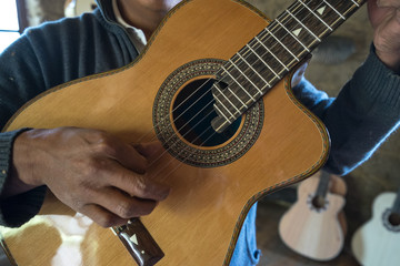 a luthier holds up a finished guitar in his small rural shop in Ecuador 