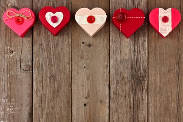 Fototapeta premium Valentines Day top border of heart shaped gift boxes with red and burlap trim over wood
