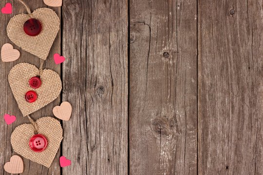 Side border of Valentines Day burlap hearts with buttons and confetti over a rustic wooden background