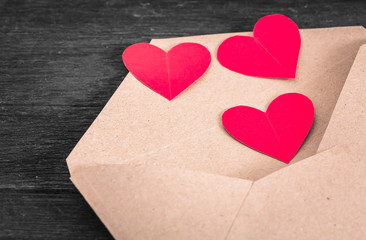Brown envelope with red paper hearts on wood background