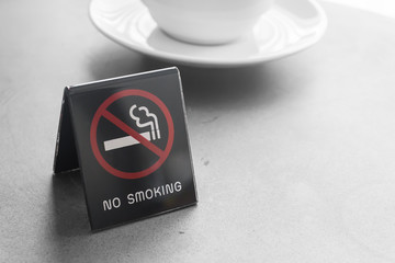 A black no smoking sign displayed with coffee cup on table