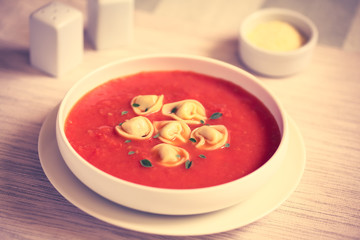 Homemade fresh cream of tomato soup with tortellini and oregano leaves, photographed with natural light (Selective Focus, Focus in the middle of the soup) (Toned Image)