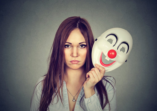 Upset worried woman with sad expression taking off clown mask