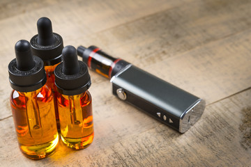 Vaping mod e-cig with tank atomizer and juice bottles over wood background
