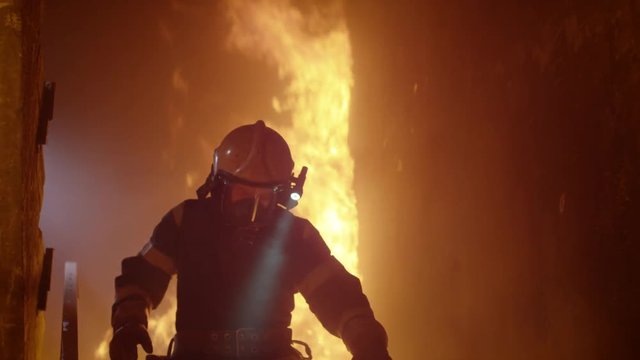 Brave Firefighter With Switched On Flashlight on His Helmet Runs Down the Burning Stairs. Fire is Raging. In Slow Motion.  Shot on RED EPIC (uhd).
