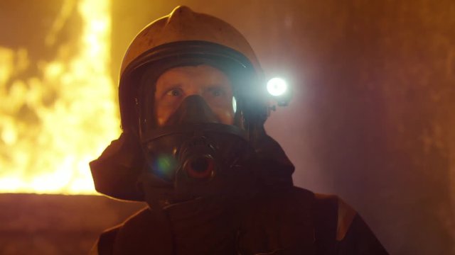 Portrait Shot of a Brave Fireman Standing in a Burning Building Fire Raging Behind Him. Open Flames and Smoke in the Background.  Shot on RED EPIC (uhd).