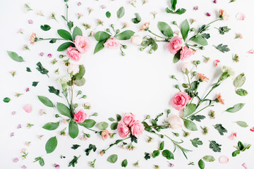 Obraz na płótnie Canvas Round frame made of pink and beige roses, green leaves, branches, floral pattern on white background. Flat lay, top view. Valentine's background