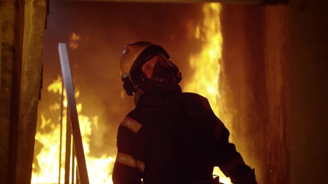 Brave Fireman Descends on Burning Stairs. Looking Around Inspecting Building. Open Flames in the Background.  Shot on RED EPIC (uhd).