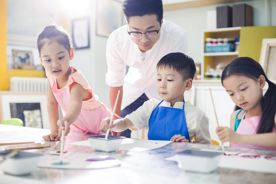 Little children painting in art class with teacher