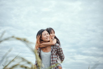 Mother giving daughter ride on back in park. Portrait of happy .