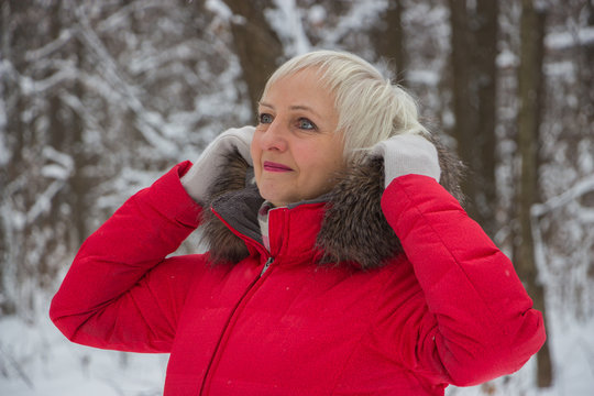 Portrait of a nice senior woman in the winter snow wood in red coat