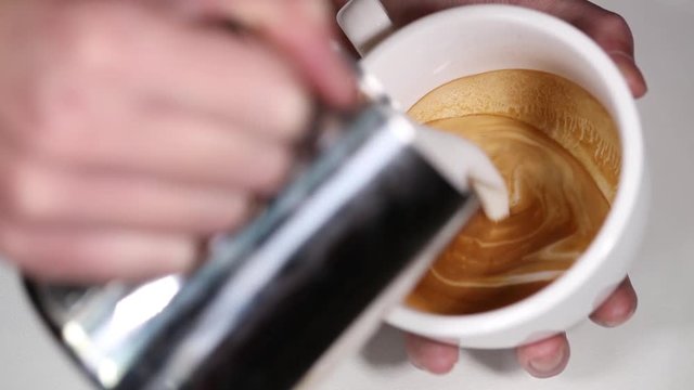 Barista draws milk over a coffee - making latte art for cappuccino