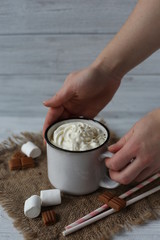 Hot chocolate with  caramel, whipped cream and marshmallow in white vintage cups on the wooden table.
