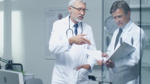 Two Specialist Doctors Discussing Patient's Log. Both are Senior and Experienced. Their Office Looks Modern and Respectable.  Shot on RED Cinema Camera in 4K (UHD).