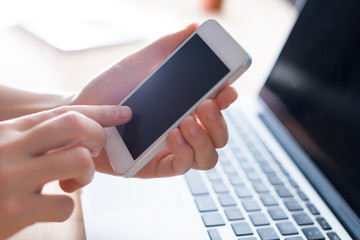 Hands using phone in front of the computer, tapping in the screen