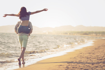 A guy carrying a girl on his back, at the beach, outdoors