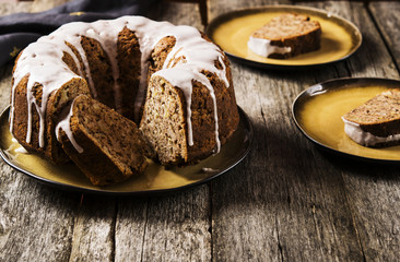 Banana cake with apples and walnuts drizzled frosting and sliced pieces on plates with effect craquelure on the shabby wooden background. Selective focus 