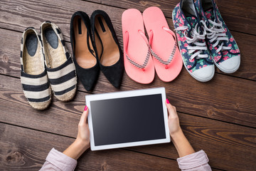 Fototapeta na wymiar Female shoes collection on wooden table with woman's hands holding white digital tablet