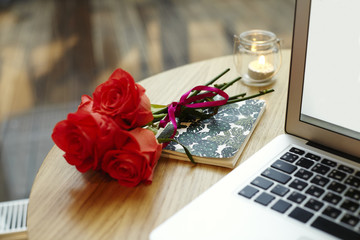 Closeup laptop screen and keyboard on wooden table. Roses red flowers present for St. Valentine's Day