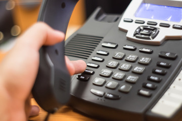 businessman dialing voip phone in the office, keyboard and monitor detail in the background with vintage color tone effect