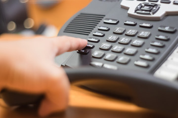 businessman dialing voip phone in the office, keyboard and monitor detail in the background with vintage color tone effect